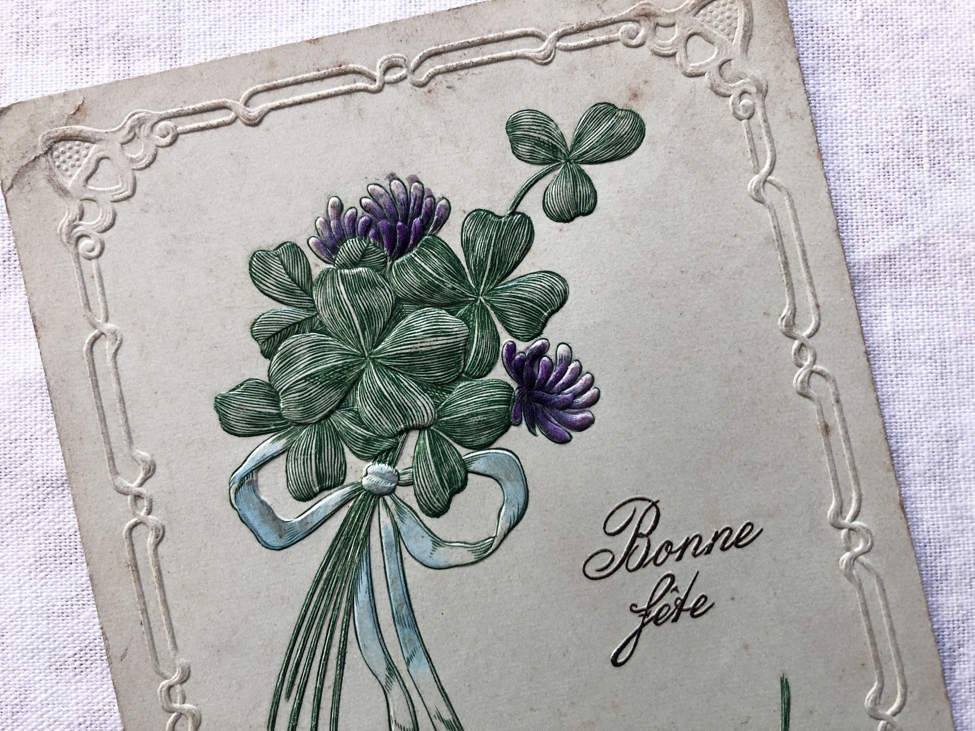 Vintage Swiss embossed postcard with a small bouquet of four-leaf clovers from 1920s.