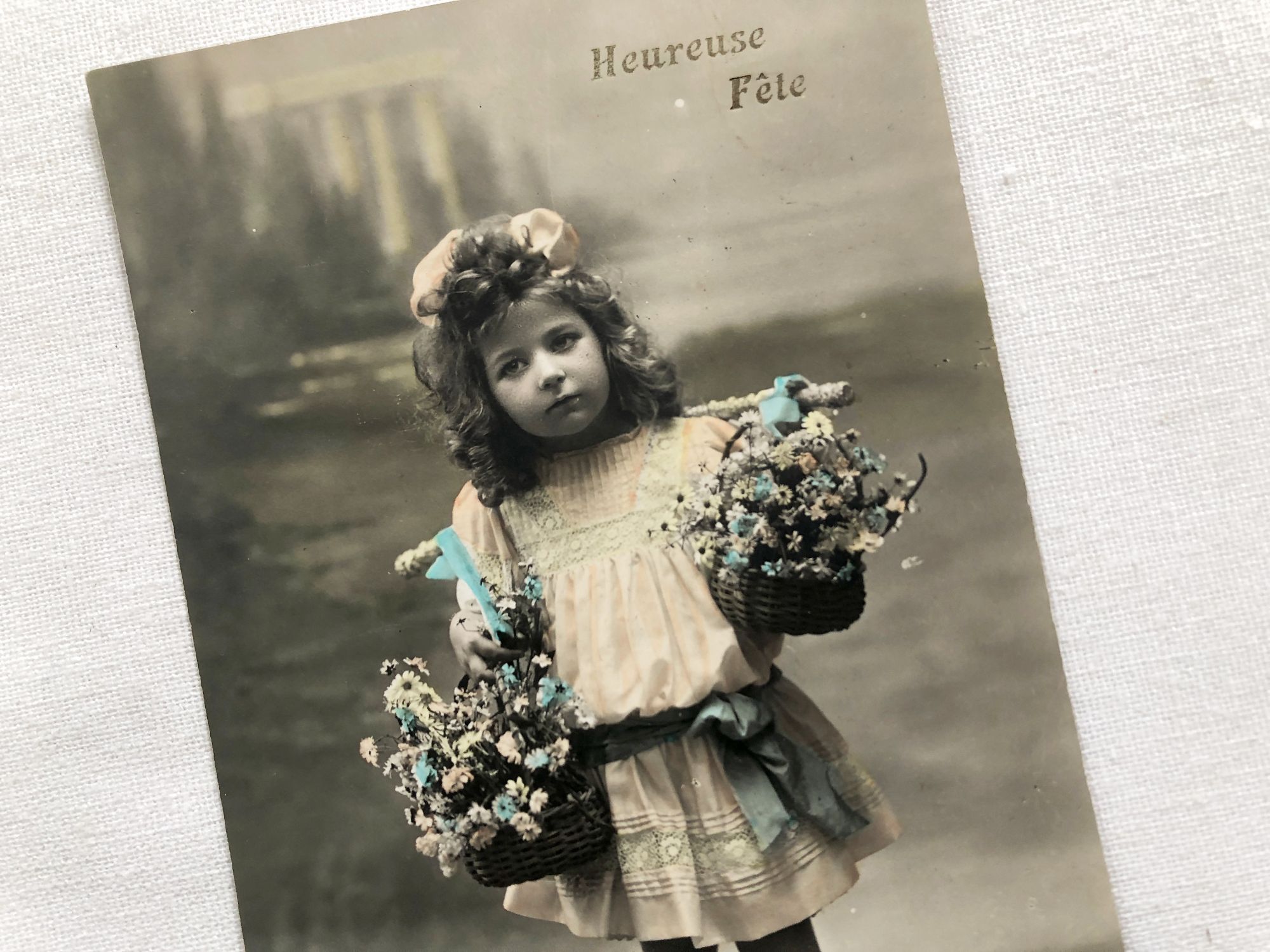 Vintage Belgian postcard with a young child with two baskets of flowers from 1910s