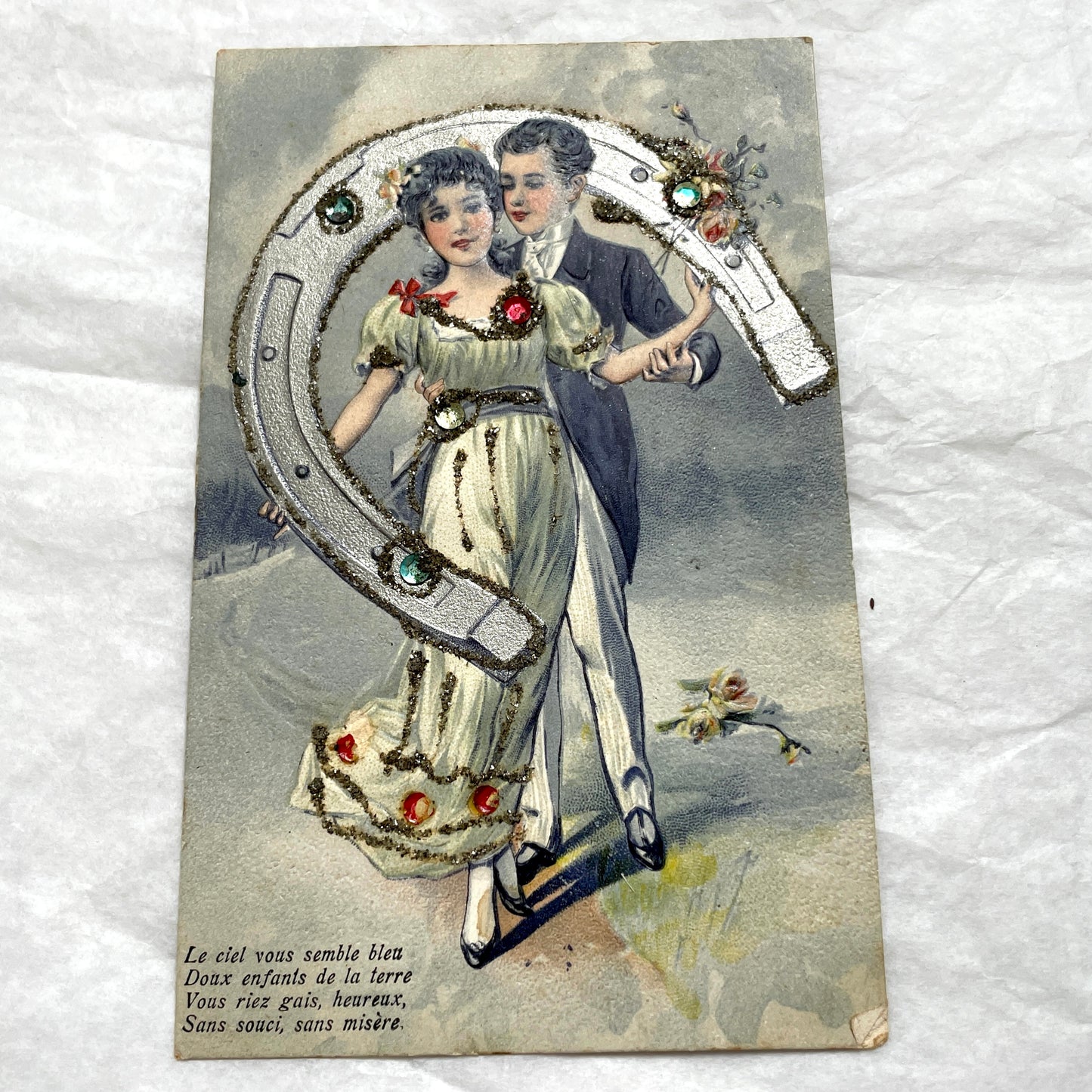 1900s French postcard with a couple holding a glitter horseshoe, adorned with small gems.