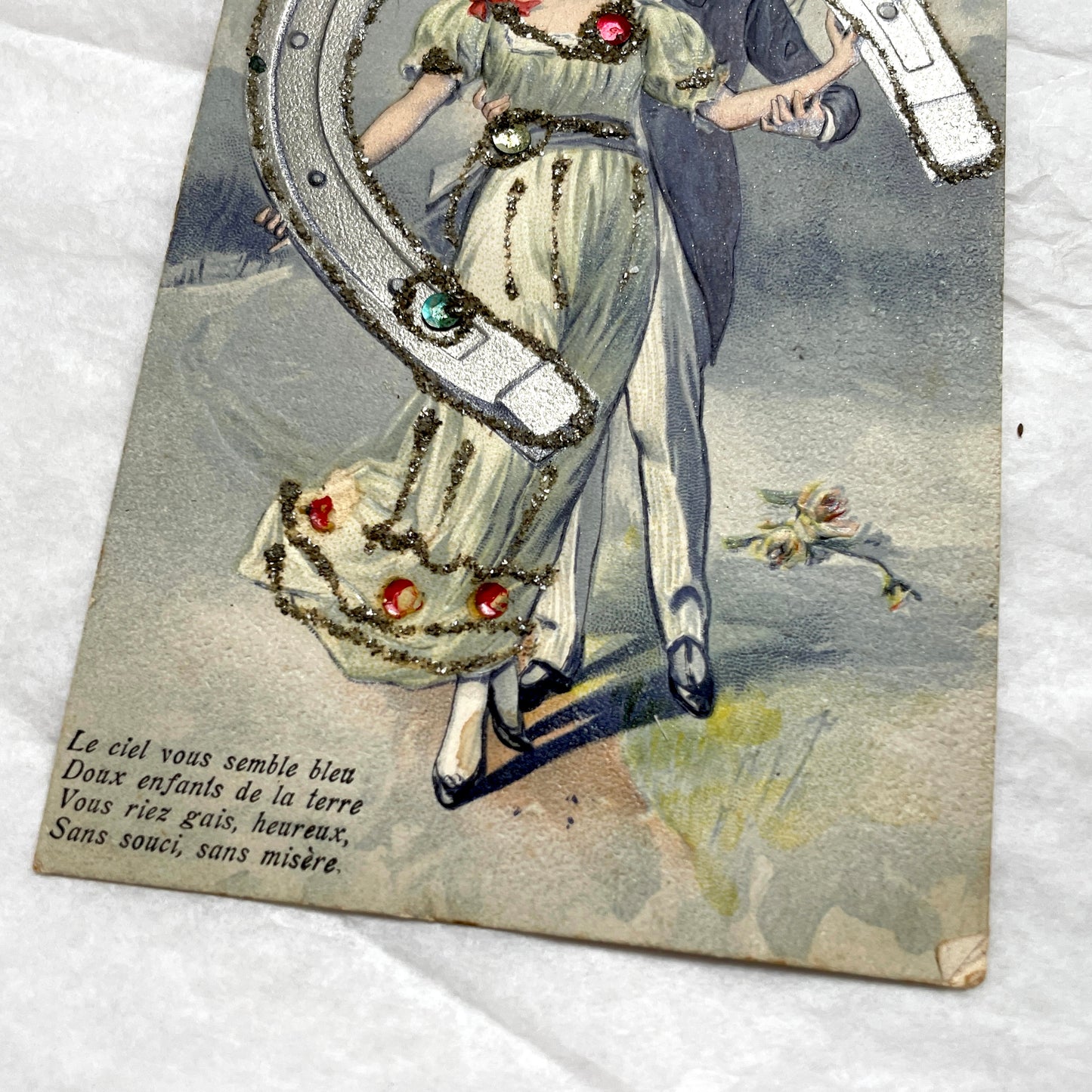 1900s French postcard with a couple holding a glitter horseshoe, adorned with small gems.