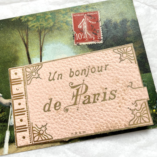 1900s French postcard featuring a Parisian lady in a pink dress, blue hat, with 'Un bonjour de Paris' text.