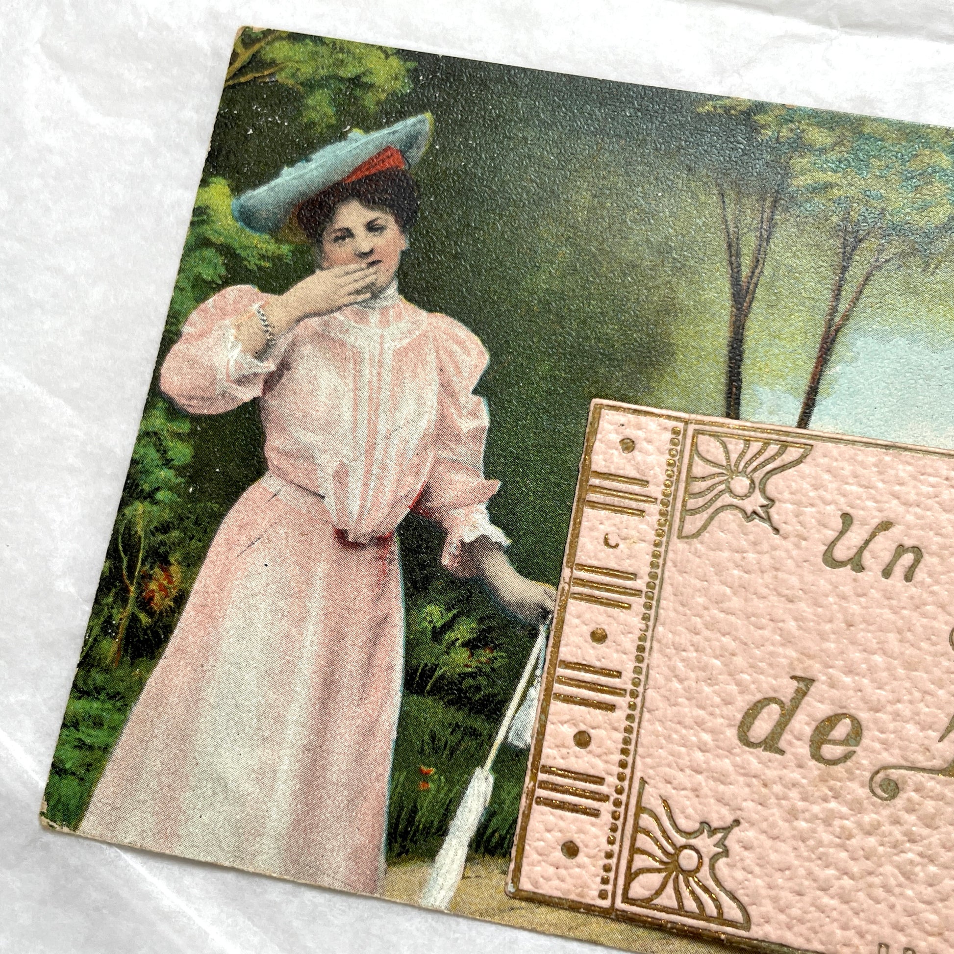 1900s French postcard featuring a Parisian lady in a pink dress, blue hat, with 'Un bonjour de Paris' text.