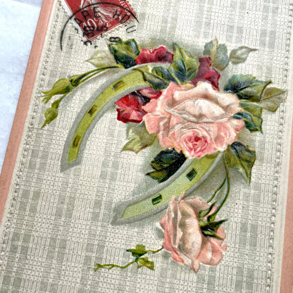 1900s French postcard with embossed pink roses and a green lucky horseshoe on a plaid background.