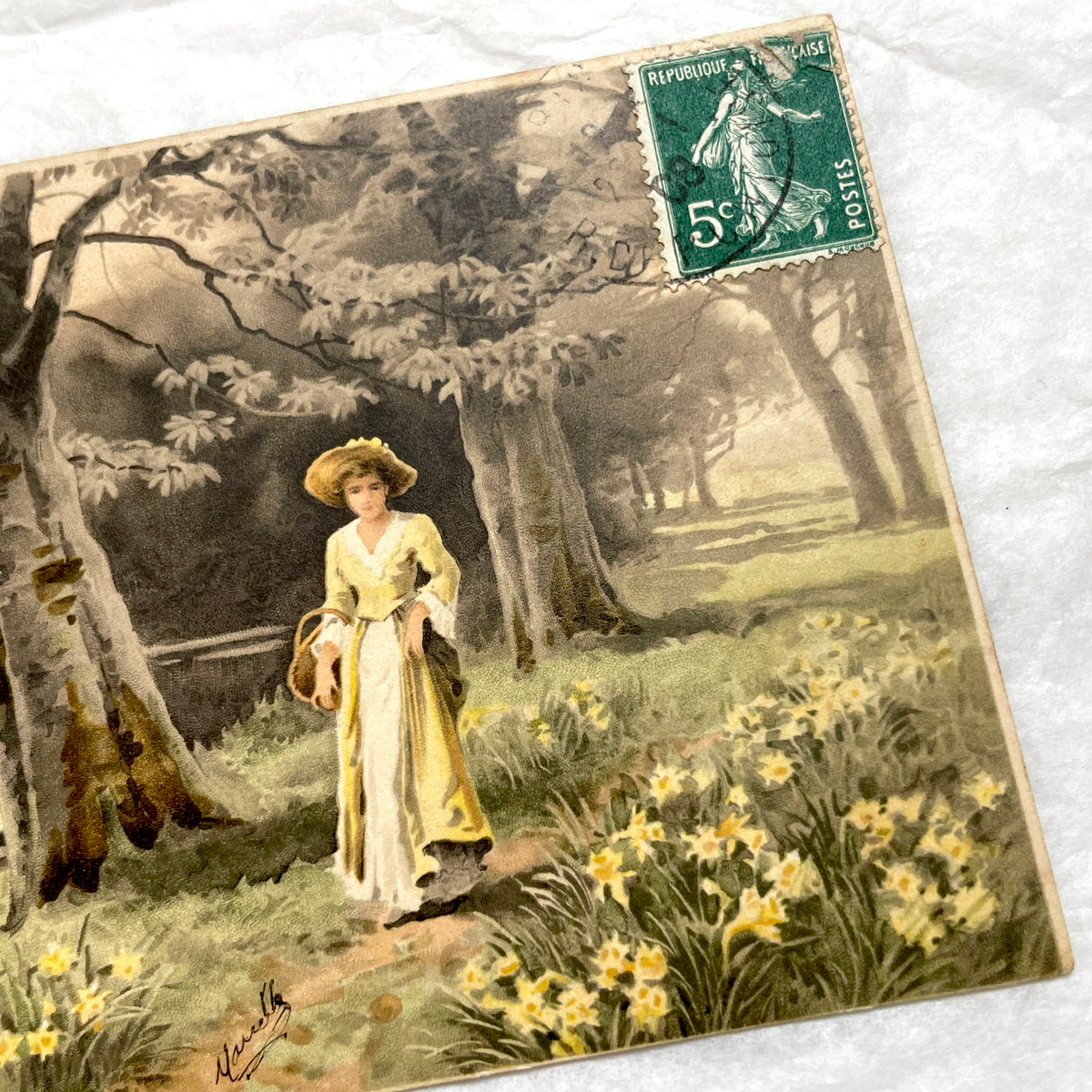 1900s French postcard depicting a woman in a yellow dress walking through a field of daffodils.
