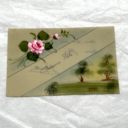 1910s French greeting card with hand-painted pink rose, green leaves, and rustic landscape scene.