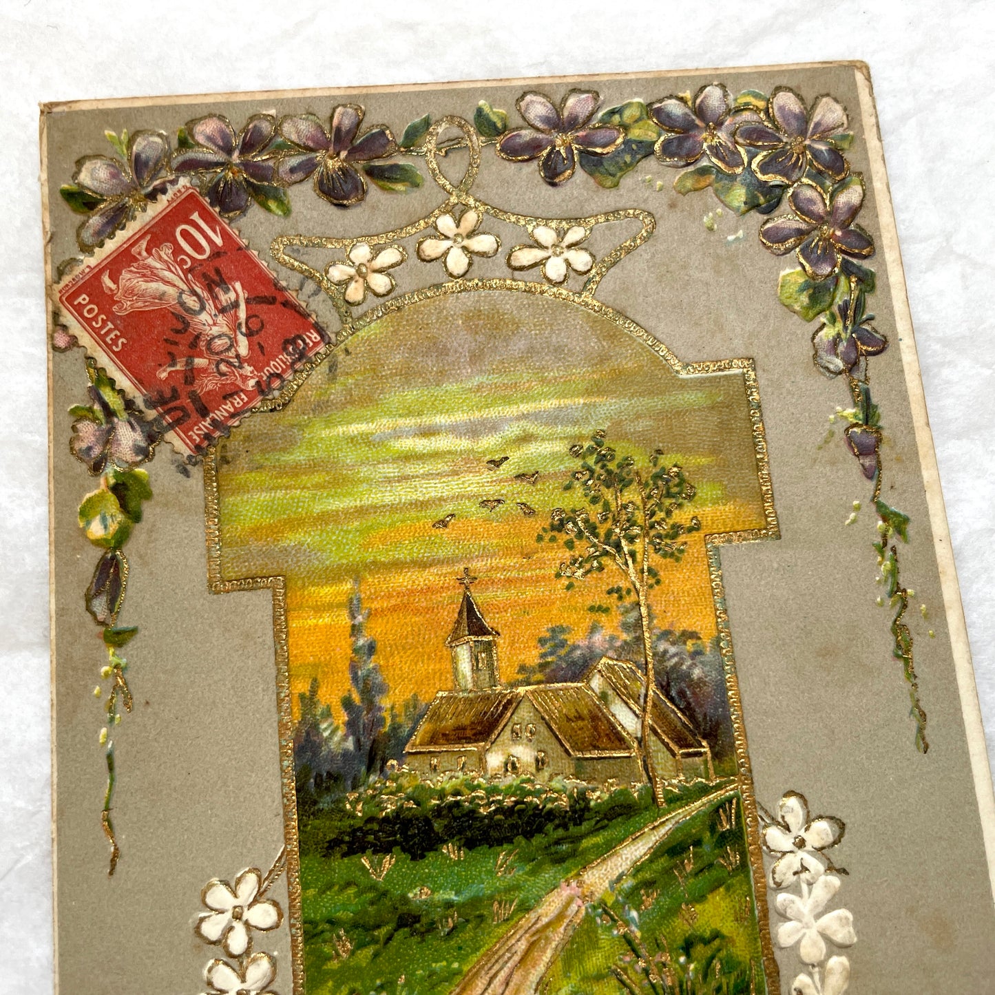 1900s French postcard featuring a gilded church landscape, floral border, and an antique 10c Postes stamp.