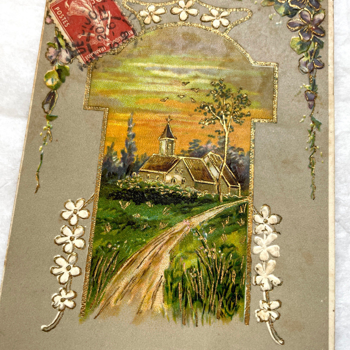 1900s French postcard featuring a gilded church landscape, floral border, and an antique 10c Postes stamp.