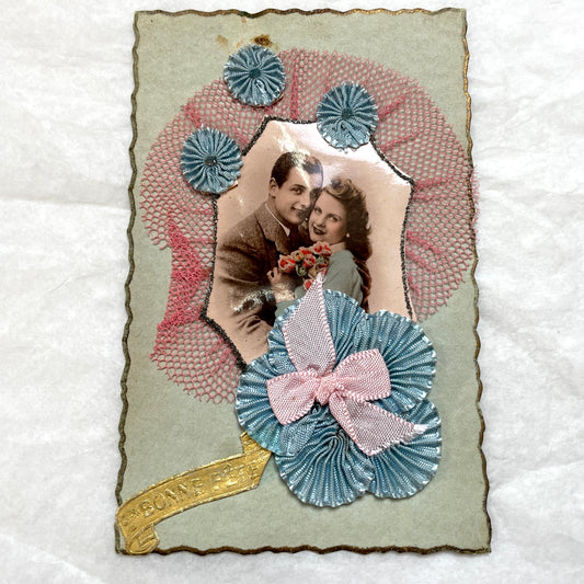1940s French greeting card featuring a romantic couple's photo, blue pleated ribbon, and 'Bonne Fête' banner.