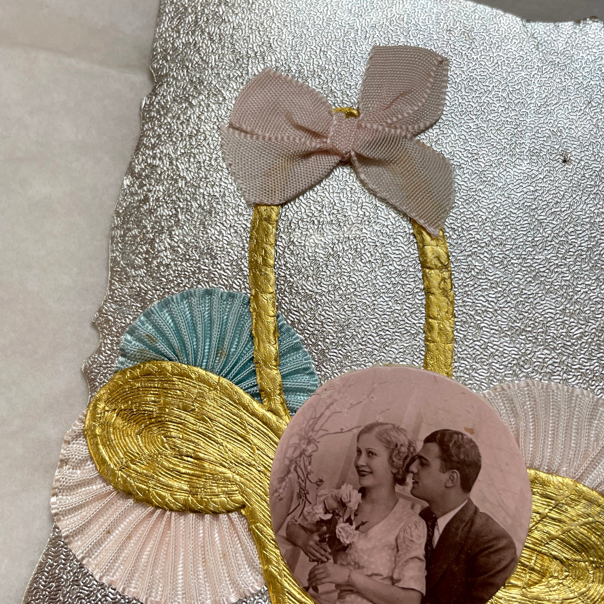 1930s vintage decorative card with a sepia wedding couple photo, golden embossed basket, and pastel ribbons on silver.
