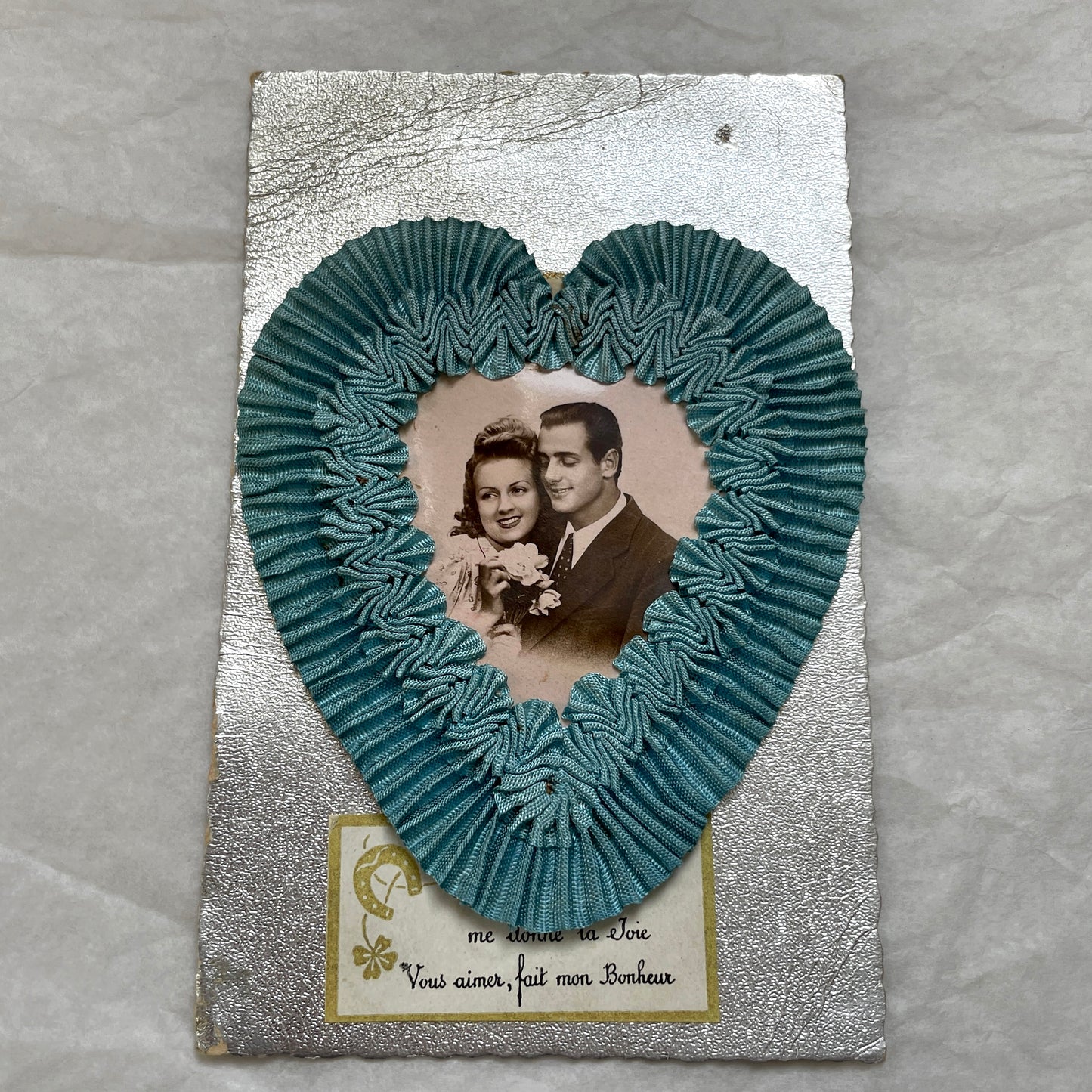 1940s French postcard with a sepia photo of a couple, framed by a blue ribbon heart and romantic French text.