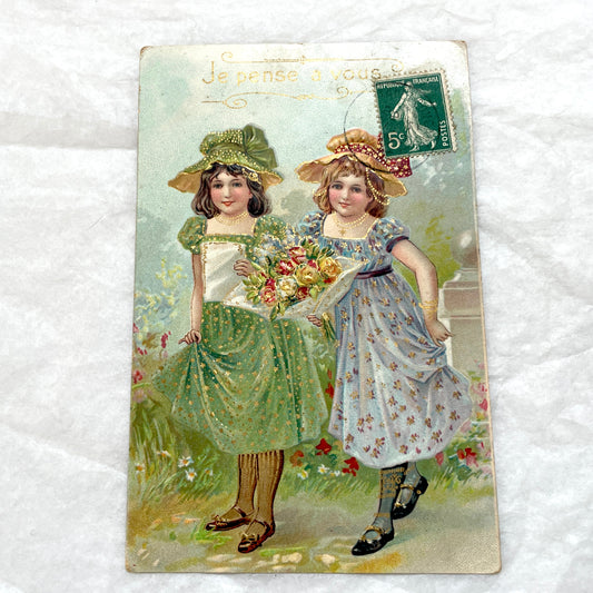 1900s postcard featuring two young girls in garden dresses with hats and a bouquet, adorned with glitter and a French stamp.