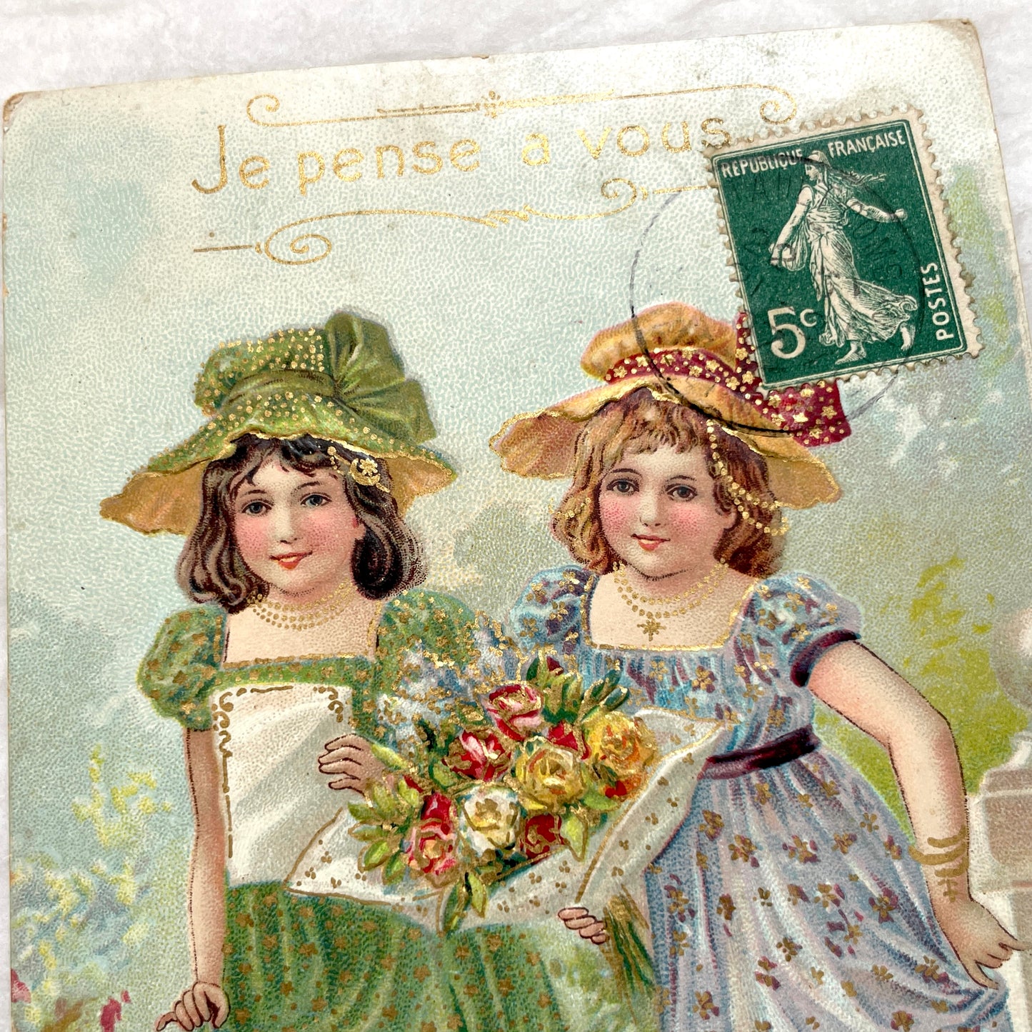 1900s postcard featuring two young girls in garden dresses with hats and a bouquet, adorned with glitter and a French stamp.