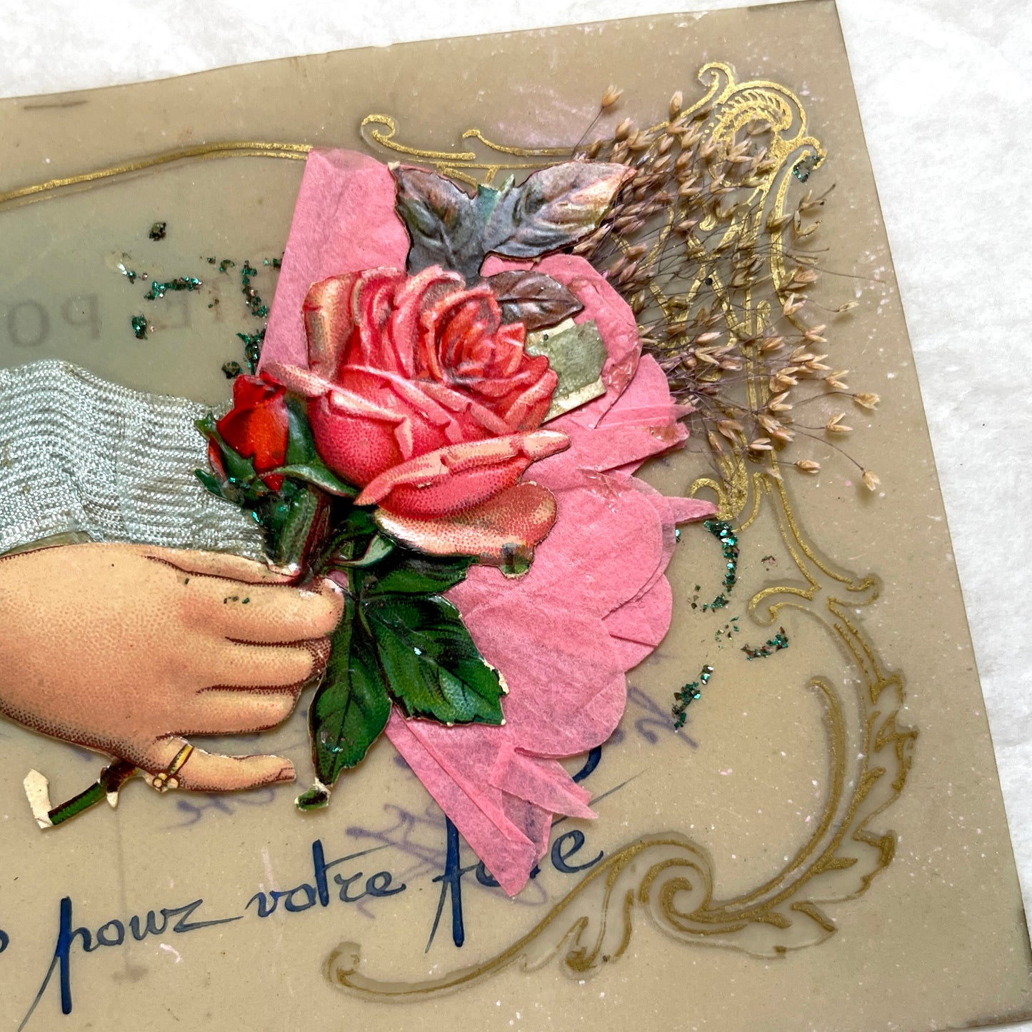 1900s French postcard with embossed hand holding pink roses, green glitter, and ornate gold frame.