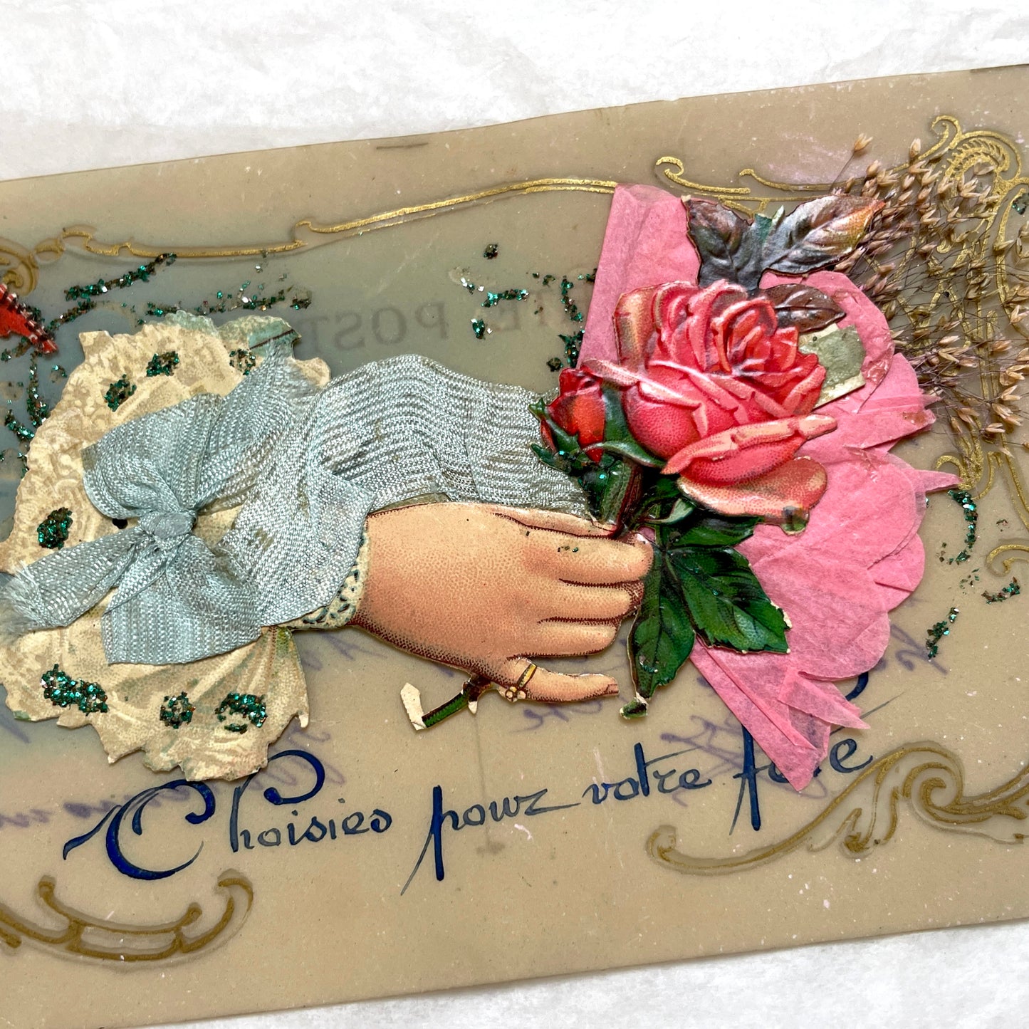 1900s French postcard with embossed hand holding pink roses, green glitter, and ornate gold frame.