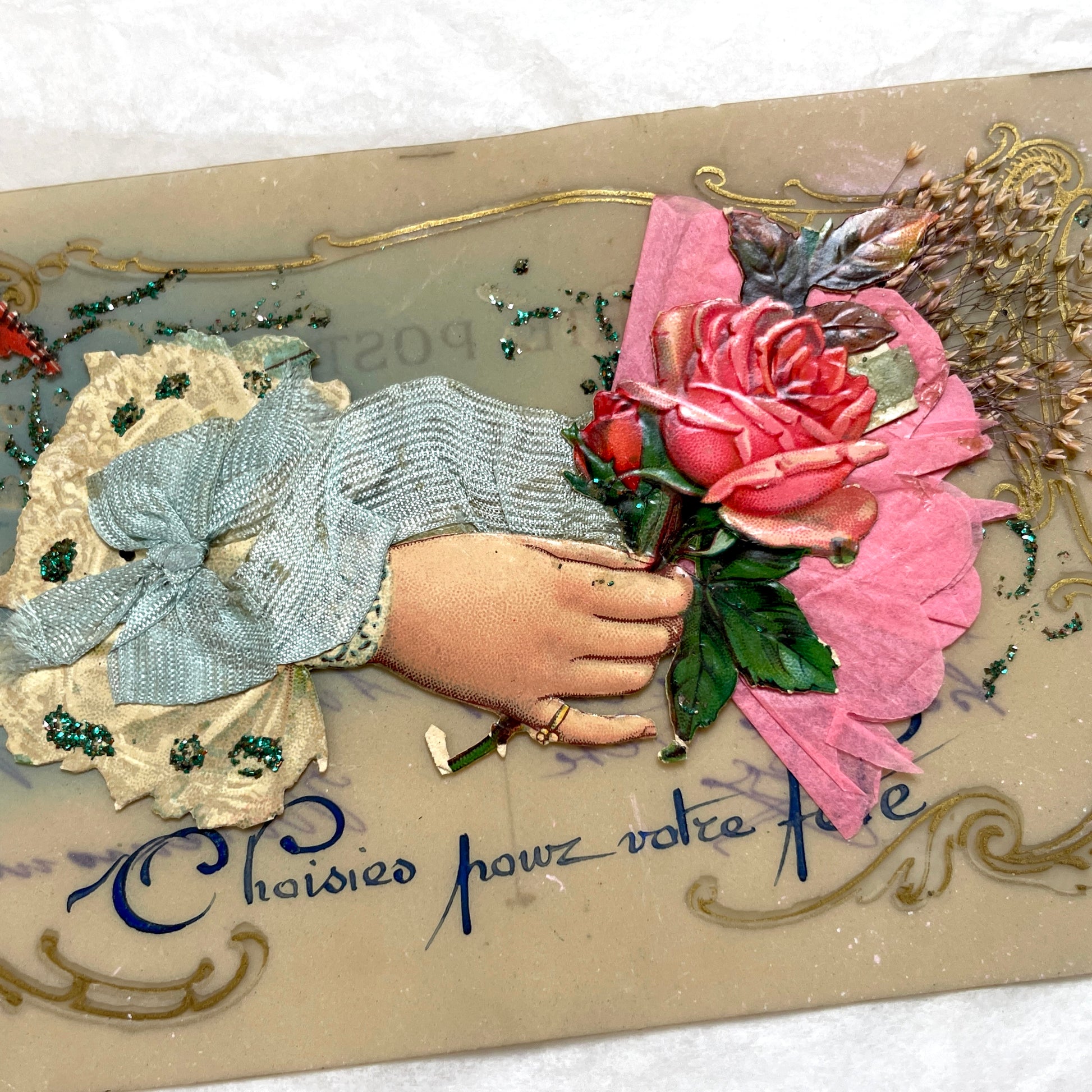 1900s French postcard with embossed hand holding pink roses, green glitter, and ornate gold frame.