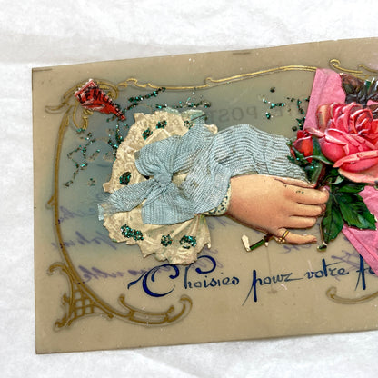1900s French postcard with embossed hand holding pink roses, green glitter, and ornate gold frame.
