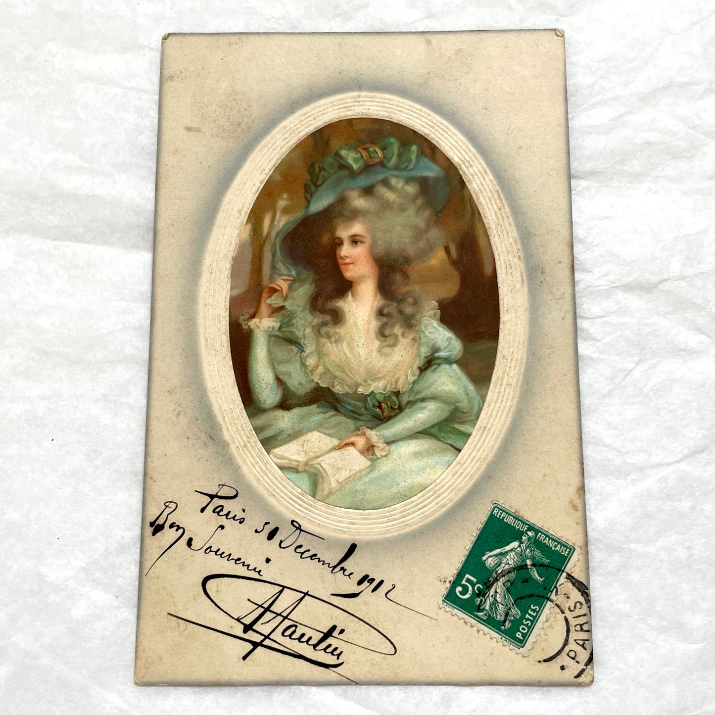 1910s French postcard depicting an elegant woman in an 18th-century teal dress and large hat, holding a book.