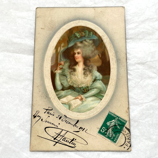 1910s French postcard depicting an elegant woman in an 18th-century teal dress and large hat, holding a book.