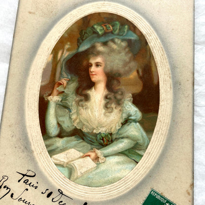 1910s French postcard depicting an elegant woman in an 18th-century teal dress and large hat, holding a book.