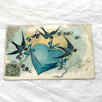 1900s French postcard with three swallows, a blue heart, blue ribbons, and flowers. Vintage ephemera.