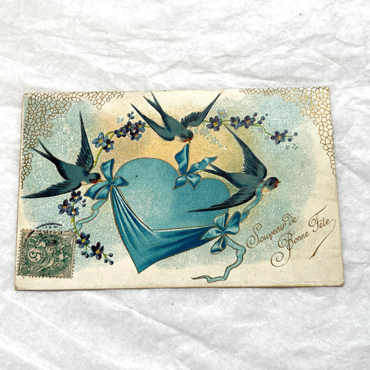 1900s French postcard with three swallows, a blue heart, blue ribbons, and flowers. Vintage ephemera.