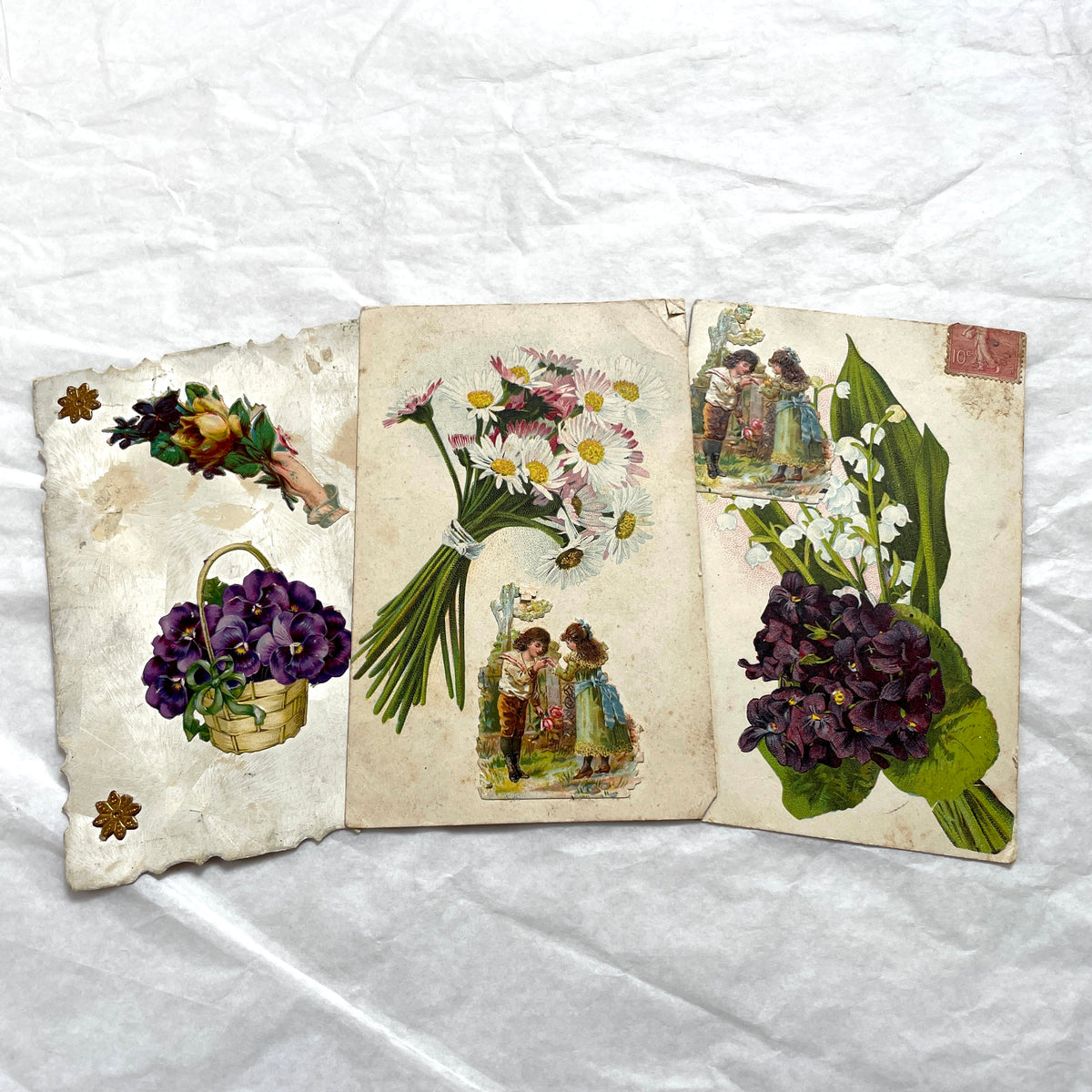 1900s lot of three antique French postcards featuring children, daisies, pansies, and lily of the valley.