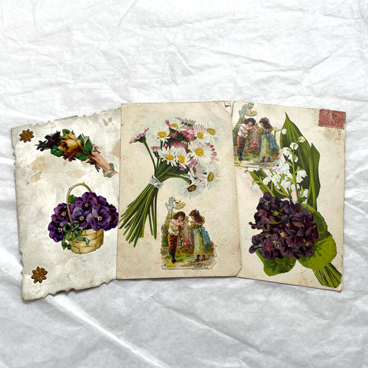 1900s lot of three antique French postcards featuring children, daisies, pansies, and lily of the valley.