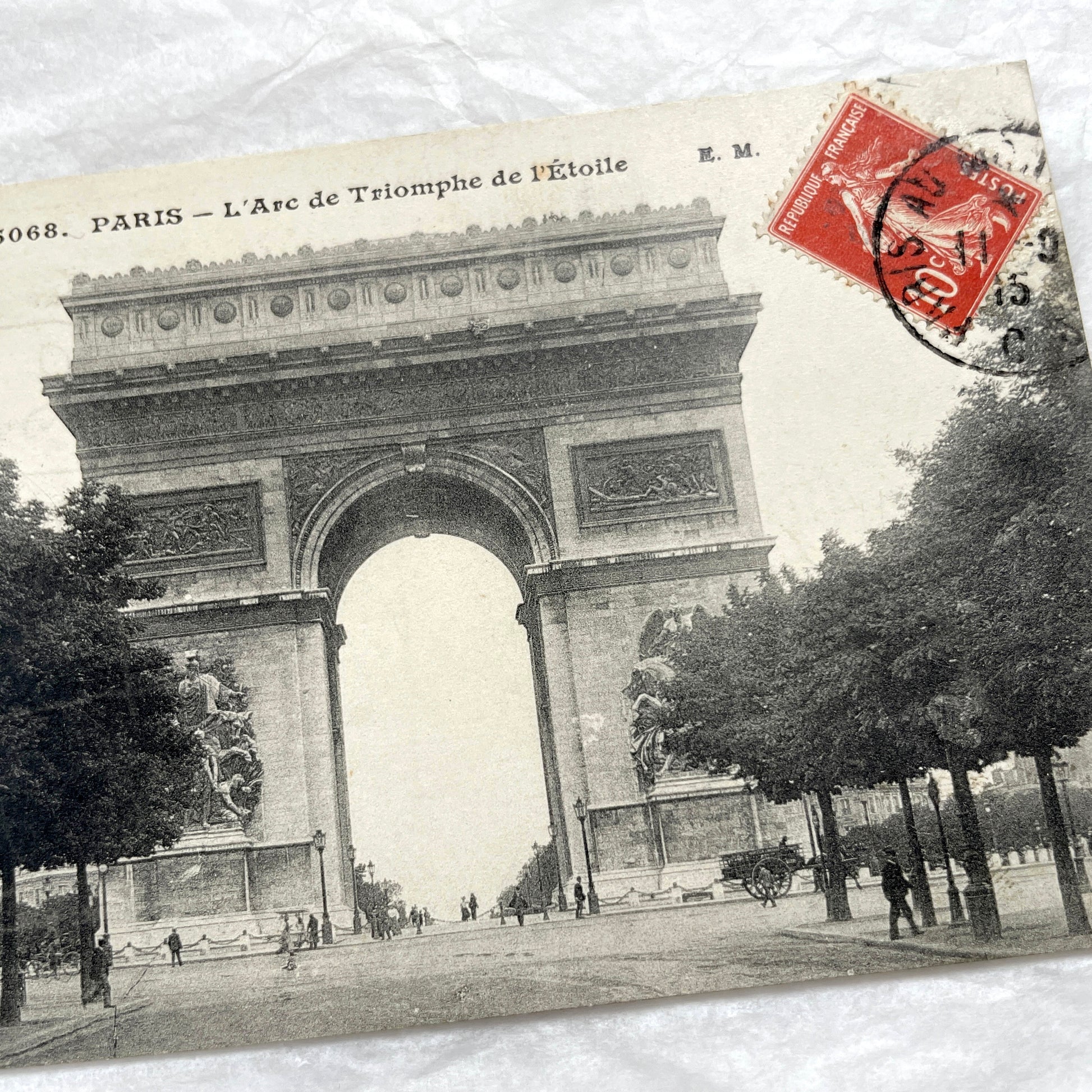 1900s postcard of Paris Arc de Triomphe with horse carriages and pedestrians on a tree-lined street.