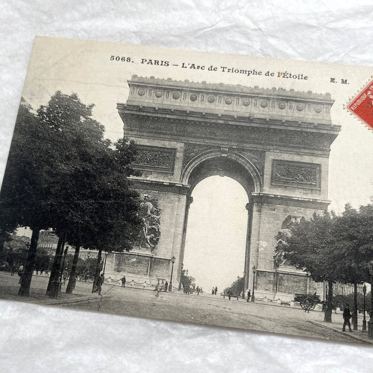 1900s postcard of Paris Arc de Triomphe with horse carriages and pedestrians on a tree-lined street.