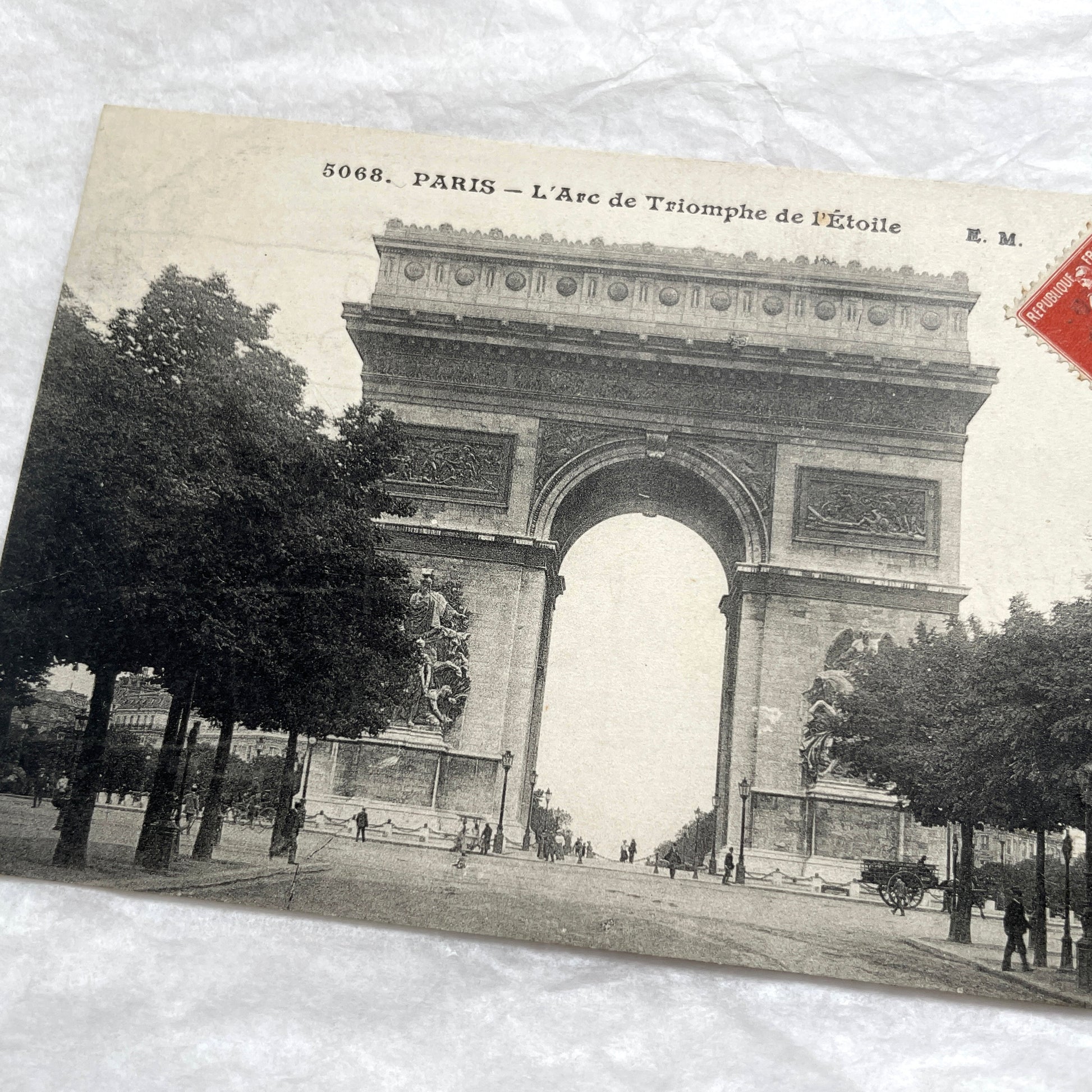 1900s postcard of Paris Arc de Triomphe with horse carriages and pedestrians on a tree-lined street.