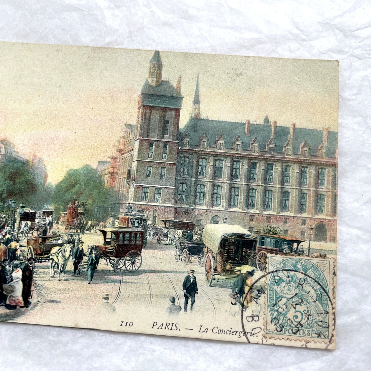 1900s French postcard depicting a bustling street scene in Paris with horse-drawn carriages and La Conciergerie.
